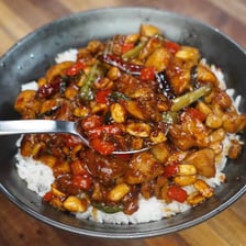 A bowl of kung pao chicken garnished with peanuts and peppers