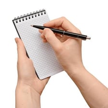 A person writing brief notes in a notebook.