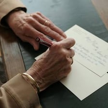 A person writing a letter to a pen pal at a desk.