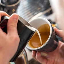 A barista pouring steamed milk into espresso to make a latte