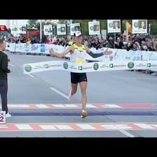 A race winner crossing a finish line ahead of competitors.