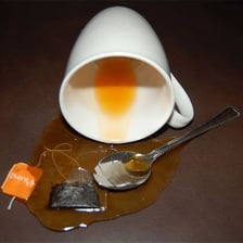 A cup of tea beside a small spill on a table