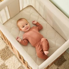 A baby sleeping in an enclosed wooden crib.