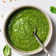 Fresh basil leaves beside a bowl of green pesto