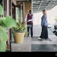 A doorman opens a doorway to let a guest inside.