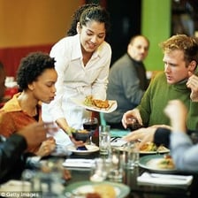 A restaurant server attending to diners at a table.