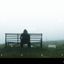 A person sitting alone in the rain with a visibly miserable posture.
