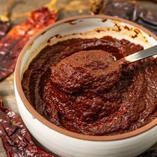A bowl of reddish Mexican adobo marinade surrounded by chiles and spices.