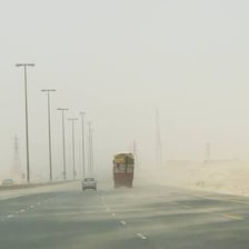 A vehicle traveling on a desert highway through blowing dust with severely reduced visibility