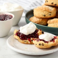 A freshly baked scone served on a plate beside a cup of tea