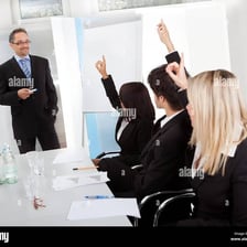 Members of a formal meeting raising their hands to vote in favor.