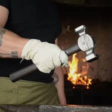 A craftsperson forging a metal hammer in a workshop.