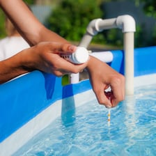 A person adding chlorine treatment to swimming-pool water.