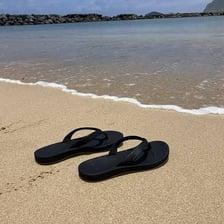 A pair of open sandals resting on sand near the beach.