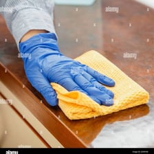 A hand using a cloth rag to wipe a tabletop.