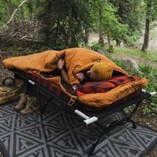 A person spreading a rolled sleeping bag flat on the ground