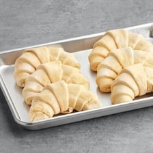 Fresh crescent-shaped French croissants arranged on a bakery tray.