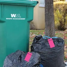 A bag of household garbage beside a trash bin