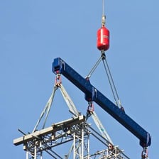 A construction crane lifting a steel beam above a building site.