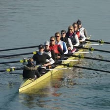 Rowers propelling narrow shells across a river.