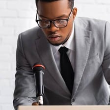 A person speaking into a microphone with a visibly strained or hoarse voice.