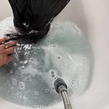 A person rinsing shampoo from their hair under running shower water.