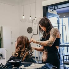 A hairstylist working on a client’s hair alongside examples of finished hairstyles