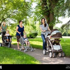A parent walking leisurely through a park while pushing a baby carriage.
