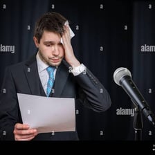 A person pausing uncertainly while speaking into a microphone.