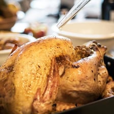 A roast turkey being brushed with cooking juices in a roasting pan