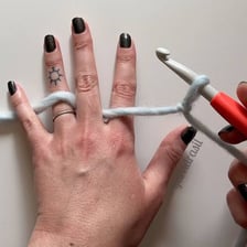 Hands using a hooked needle to crochet yarn
