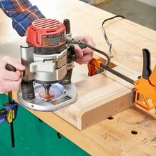 A woodworker using a handheld router to shape a wooden board.