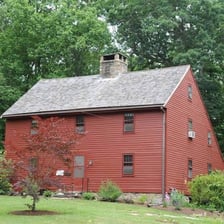 A historic saltbox house with a short front roof slope and a long rear slope.