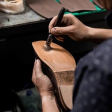 A cobbler replacing the worn sole of a shoe.