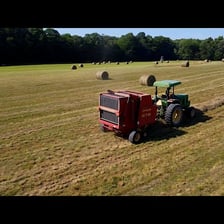 A farmer or machine compressing cut hay into bales in a field.