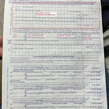 A car owner holding a vehicle title document beside a car.