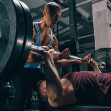 Two spotters standing ready to assist someone lifting a barbell on a bench.
