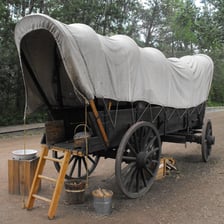 A covered wagon on an open prairie, representing the prairie schooner of the American Old West.