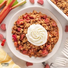 A rhubarb crumble served in a dish, with red rhubarb stalks nearby.