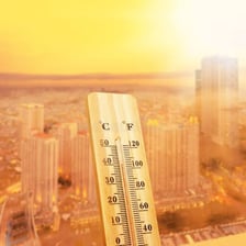 A city street shimmering in extreme heat beside a high thermometer reading