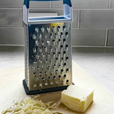 Cheese being rubbed over a box grater into fine shreds