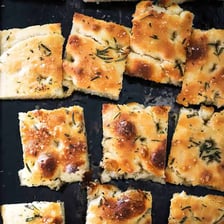 A flat Italian focaccia loaf with dimples, olive oil and herbs
