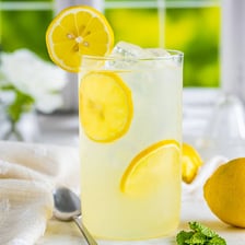 A glass of pale lemonade beside fresh lemons