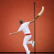 A Basque pelota player using a curved cesta on a court.
