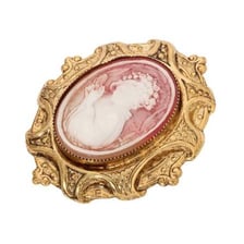 A carved cameo brooch displayed beside decorative cameo-style pottery