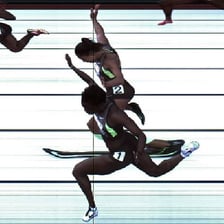 Two runners reaching a finish line together.