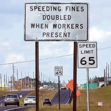 A car traveling quickly beside a highway speed-limit sign
