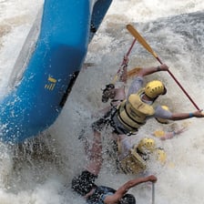 People guiding a raft with long poles on a shallow river.