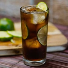 A glass of rum mixed with cola and garnished with lime