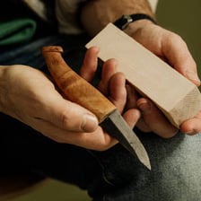 A person trimming a piece of wood with a carving knife.
